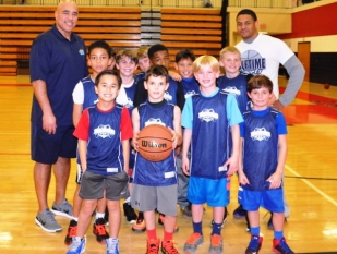 9 year old boys basketball team posing on court with coaches